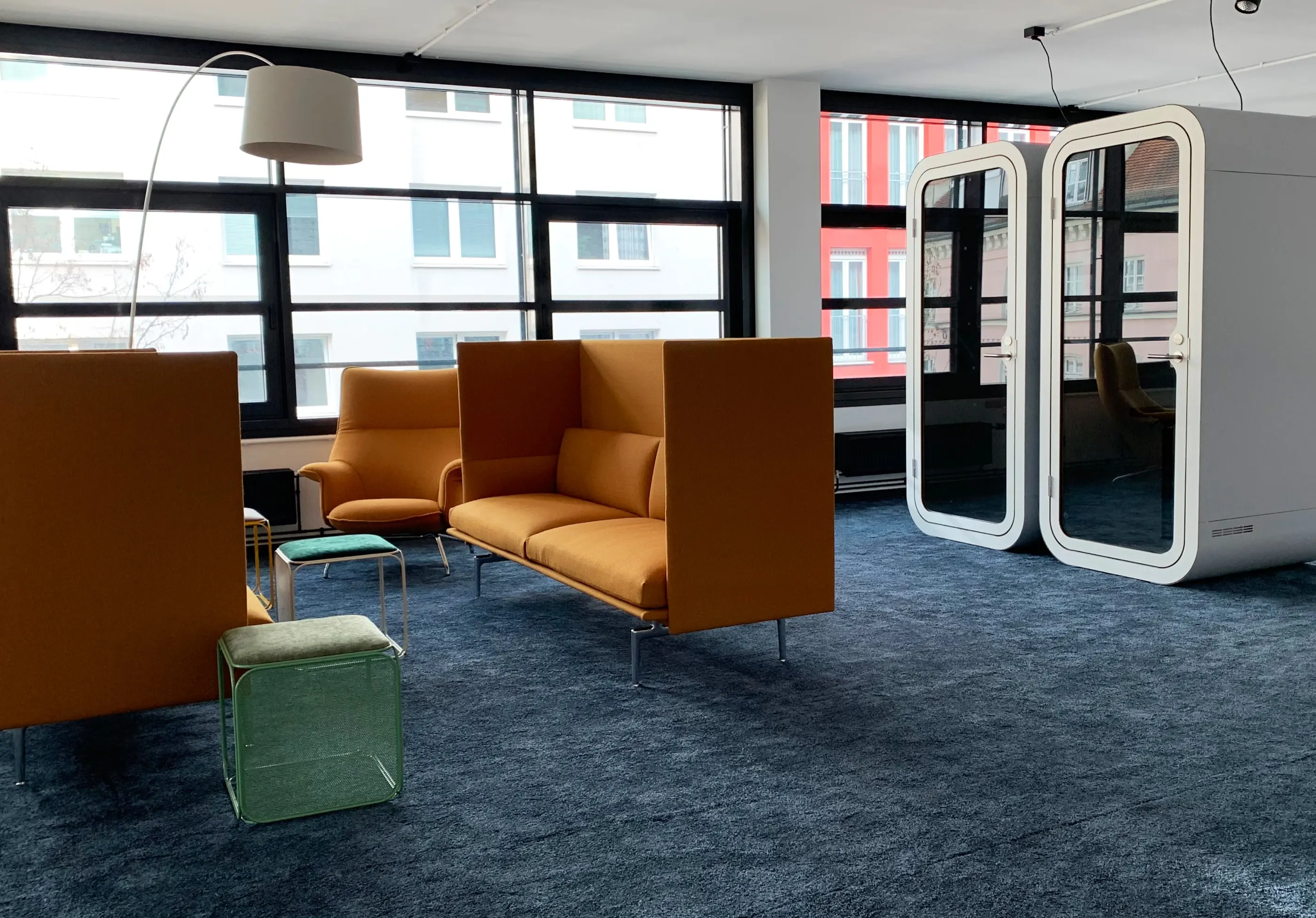Lounge with orange high-back sofas, blue carpet and two phone booths