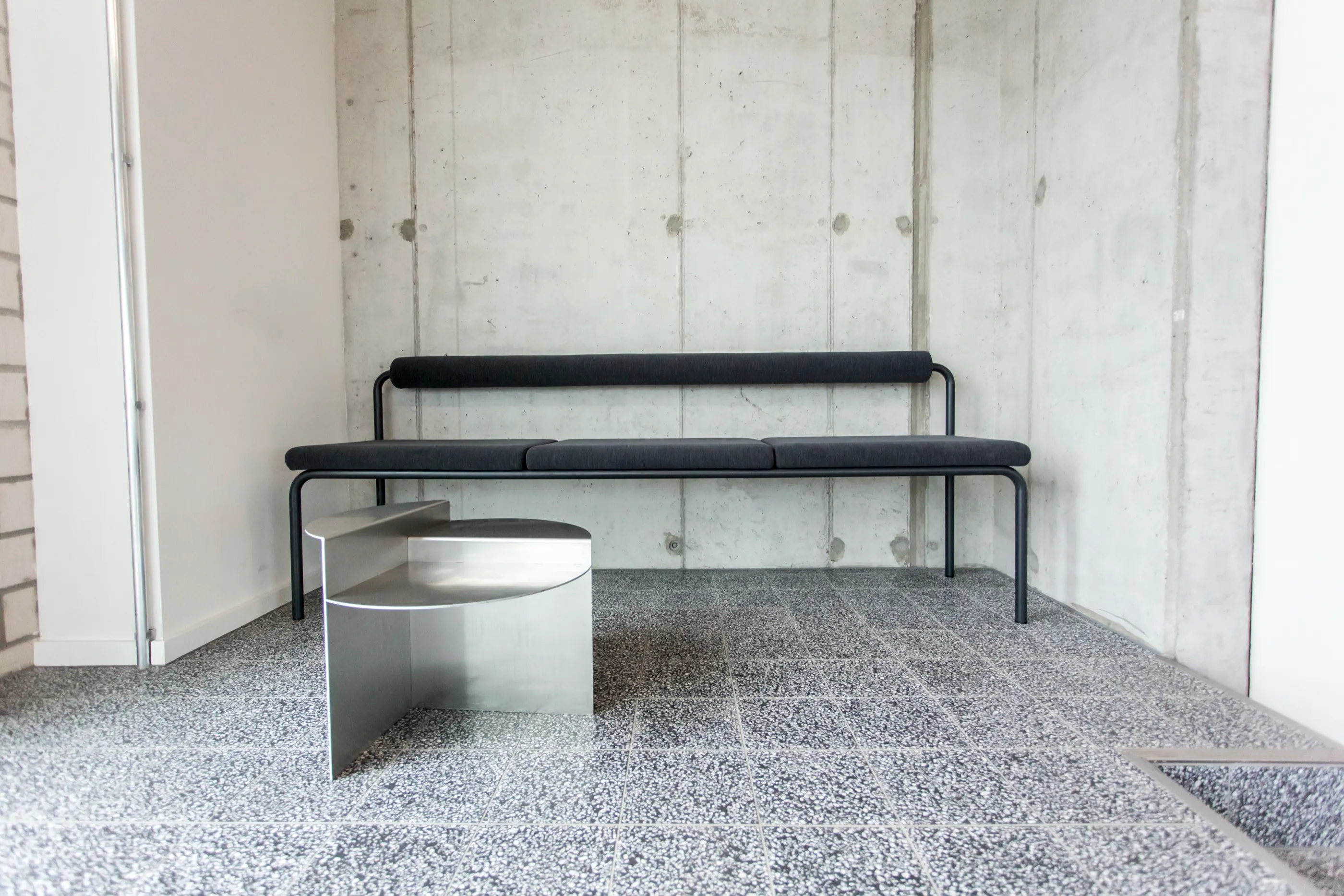 Lobby with board-marked concrete wall, terrazzo floor and a long black bench