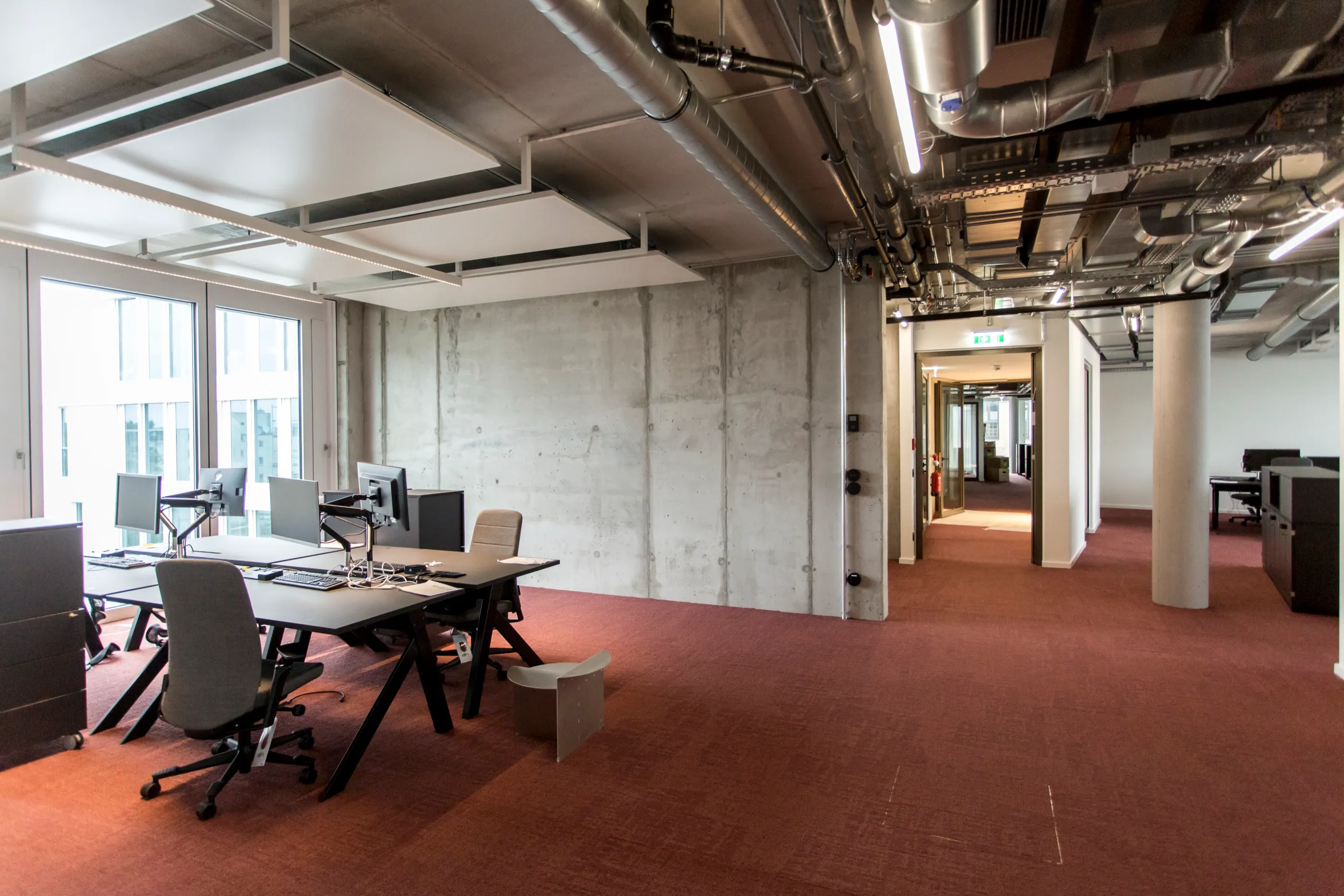 Open-plan workspace with exposed ceiling services and a concrete wall