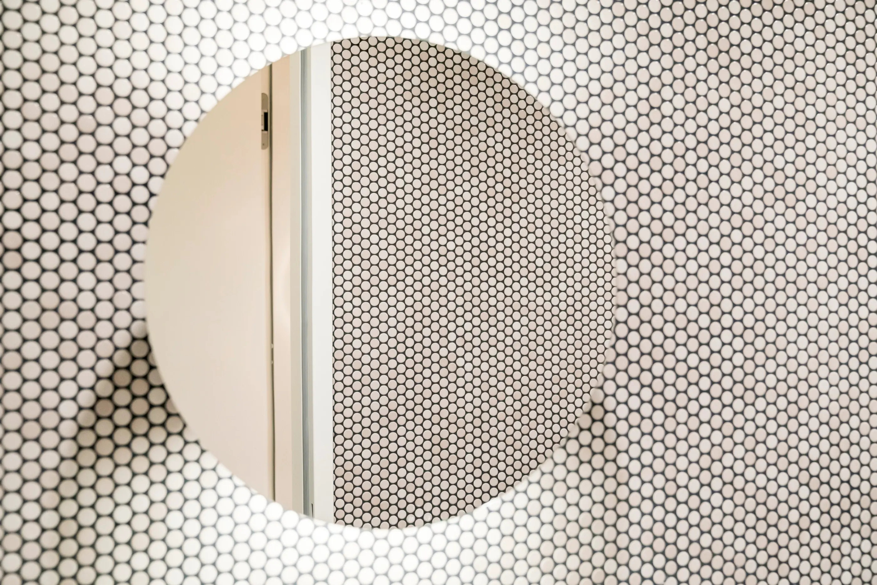 Round mirror on a wall of white penny-round mosaic tiles