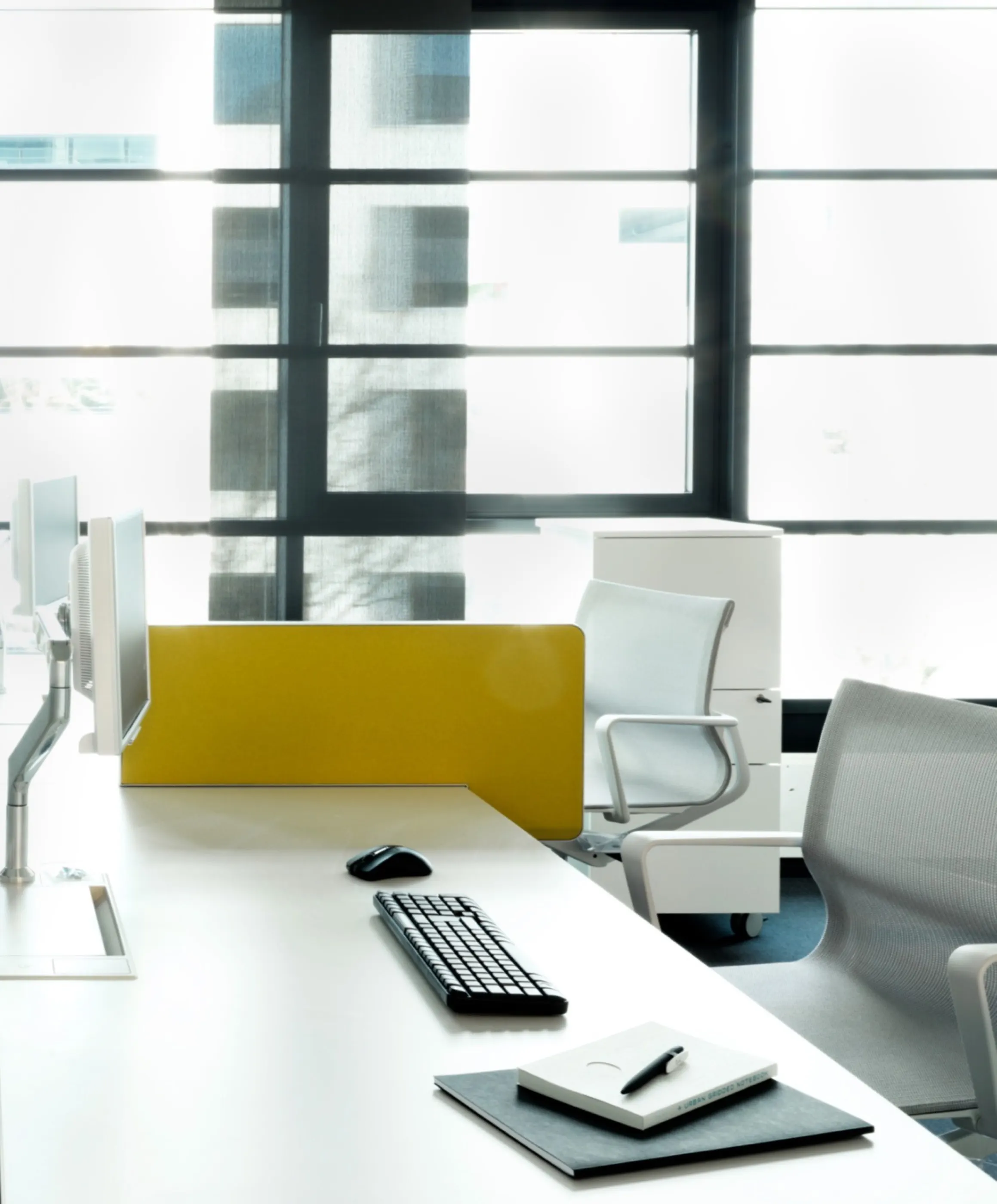 Desk with monitor arm and a yellow acoustic screen at the window